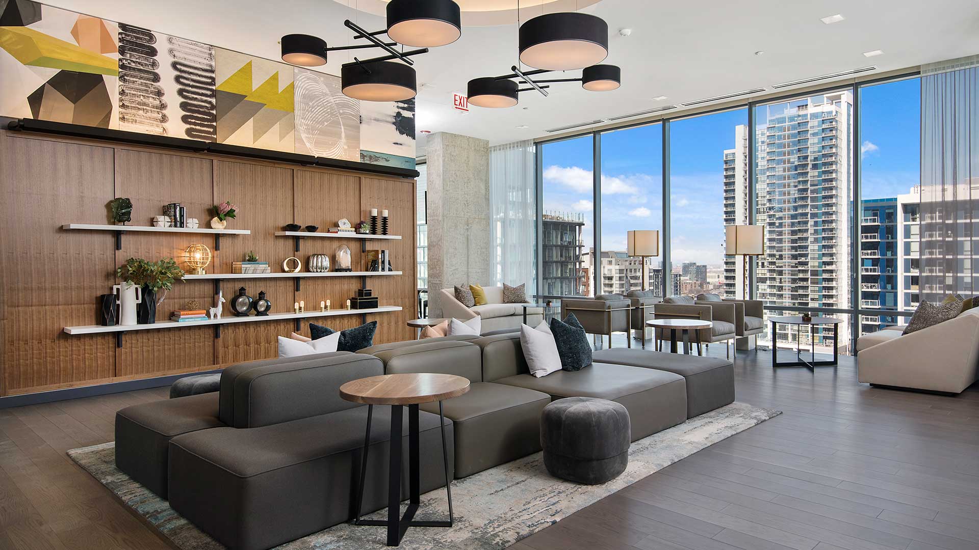 The main lounge area of the Hubbard221 amenity deck. A large section couch is in the middle with seating on both sides. Behind it is a series of wall-mounted shelves with various décor. To the right are smaller seating areas along the floor-to-ceiling windows.