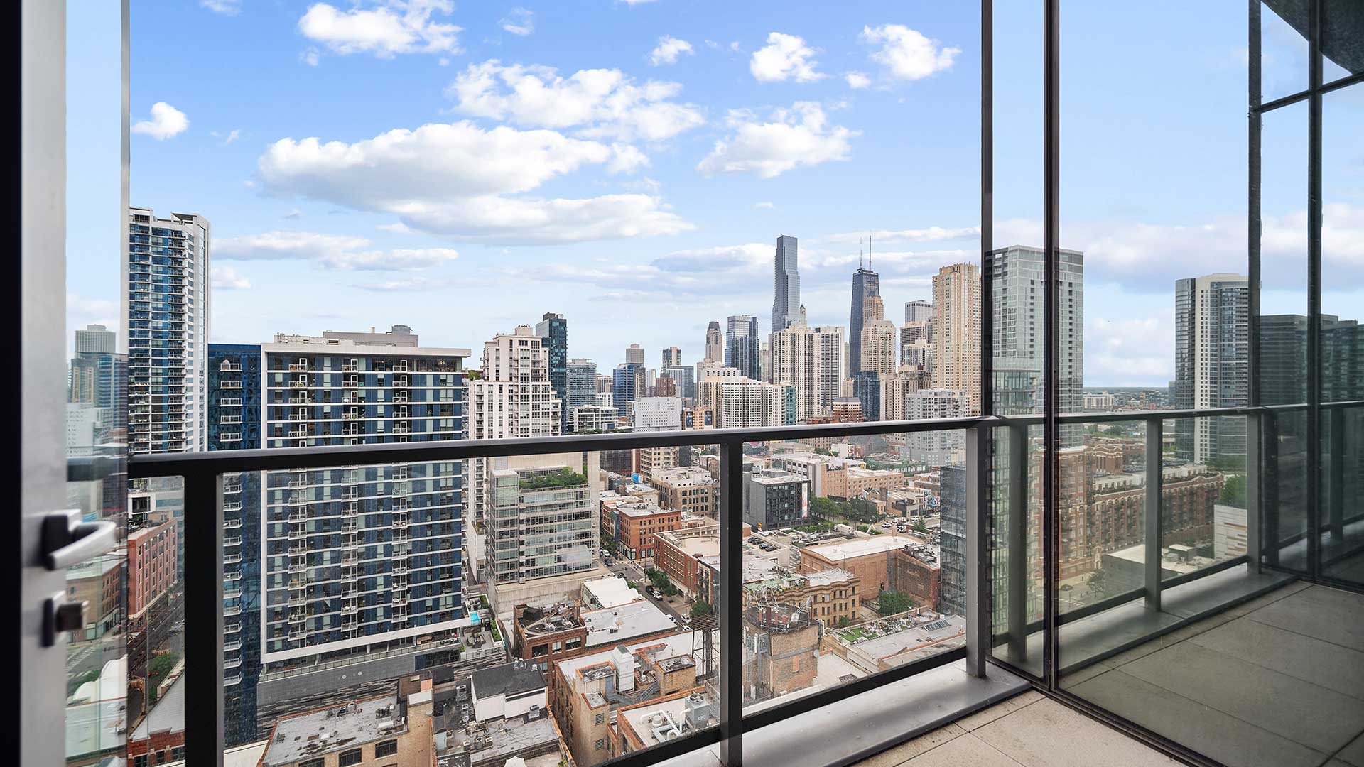 Looking out at the Chicago skyline from a residence balcony. There is a glass railing at the edge and a floor-to-ceiling window on the right.